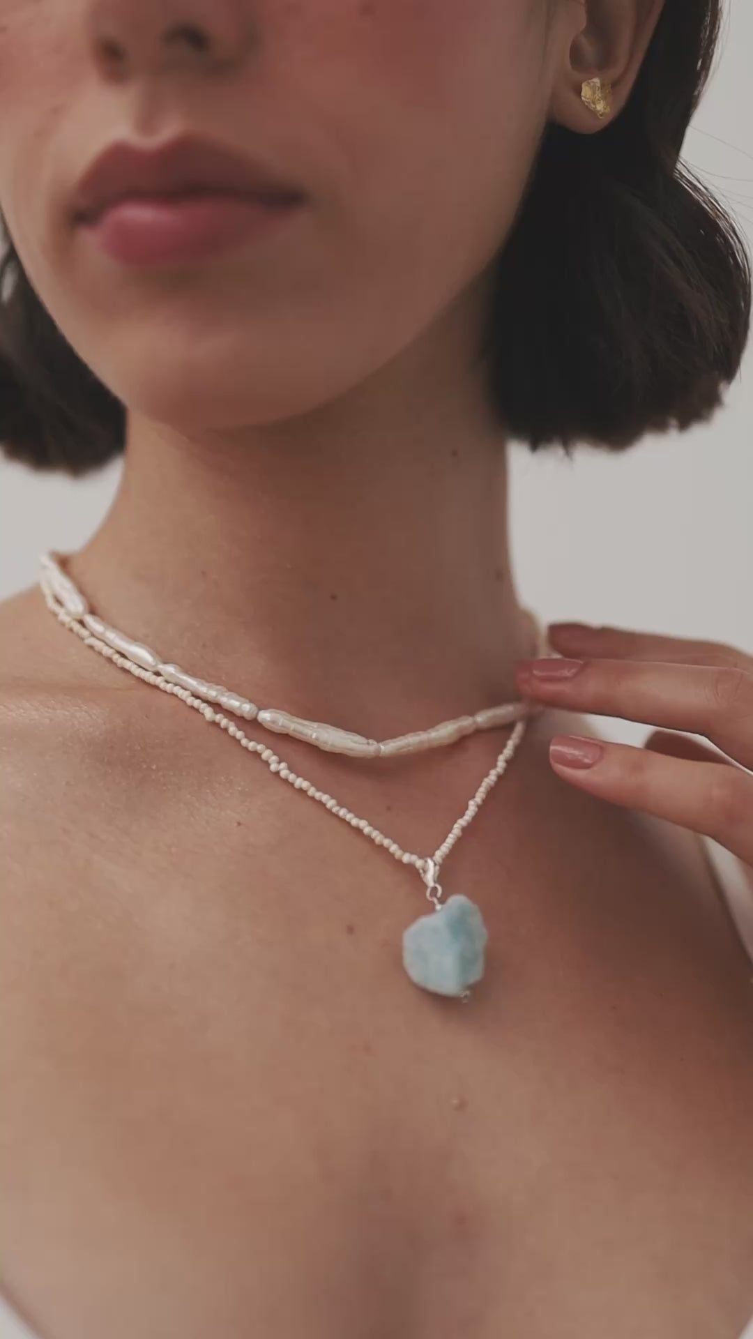 Load video: Girl wearing two pearl necklaces and a sweet nostalgic look on her face playing with the camera